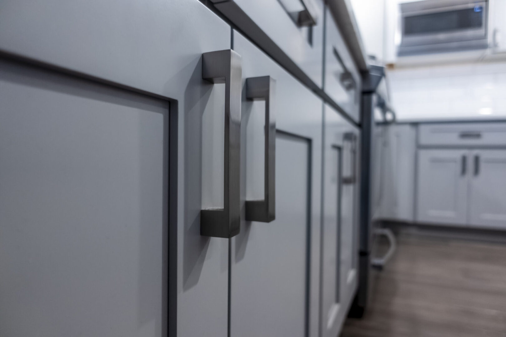 Low angle view of gray kitchen cabinet door handles inside a large, beautiful kitchen with finished, hardwood floors